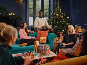 Eine Familie sitzt im Wohnzimmer und feiert Weihnachten, auf dem Tisch liegen Geschenke.